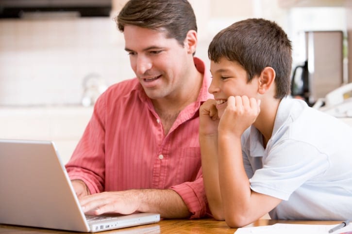 Man helping young boy in kitchen with laptop